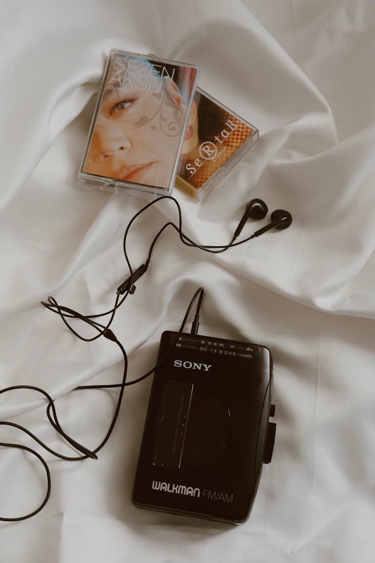 A classic Sony Walkman with cassette tapes and earphones on a white bed, showcasing retro vibes.