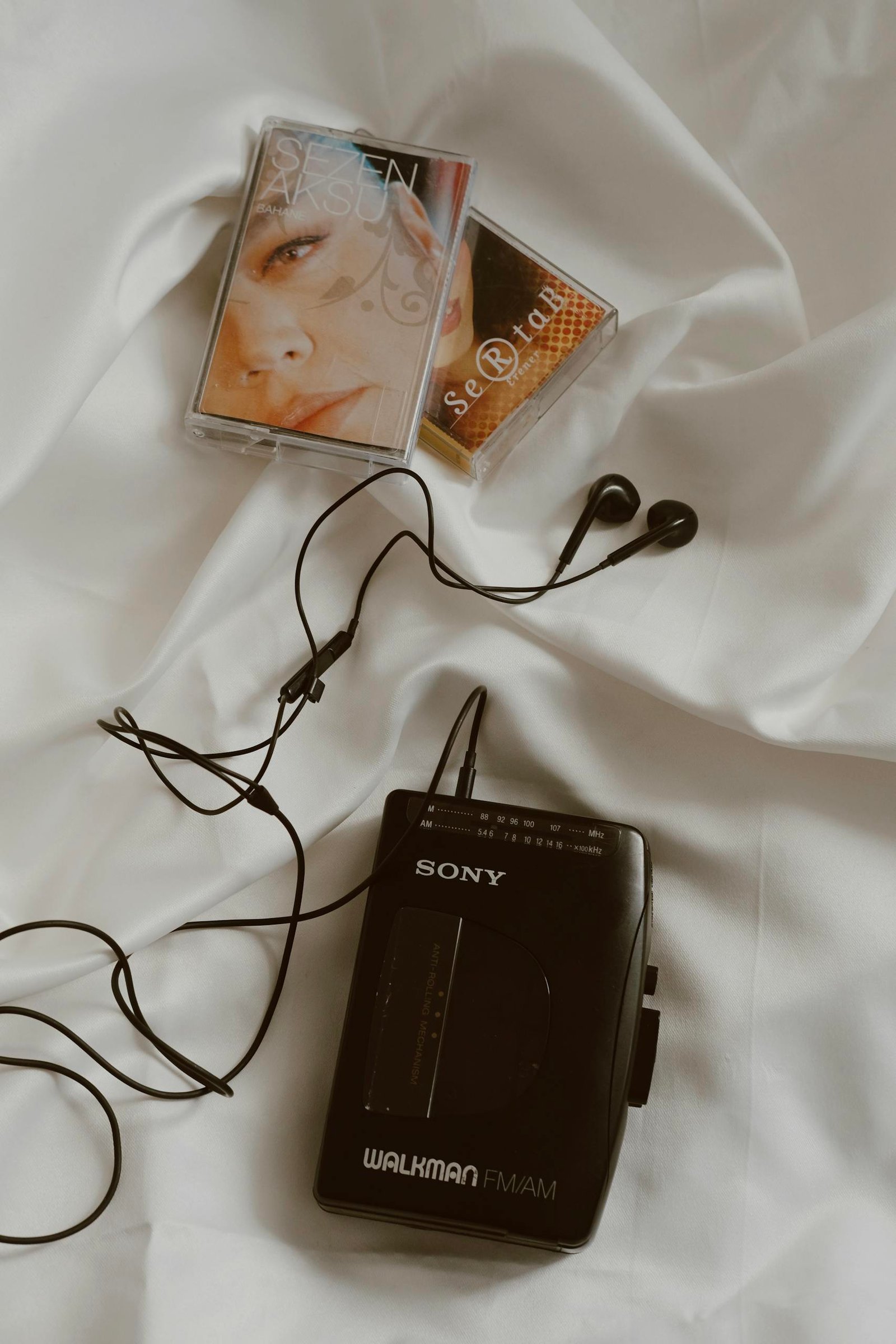 A classic Sony Walkman with cassette tapes and earphones on a white bed, showcasing retro vibes.